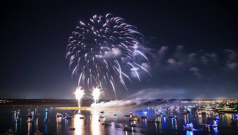 Fireworks in the sky above a river filled with boats.