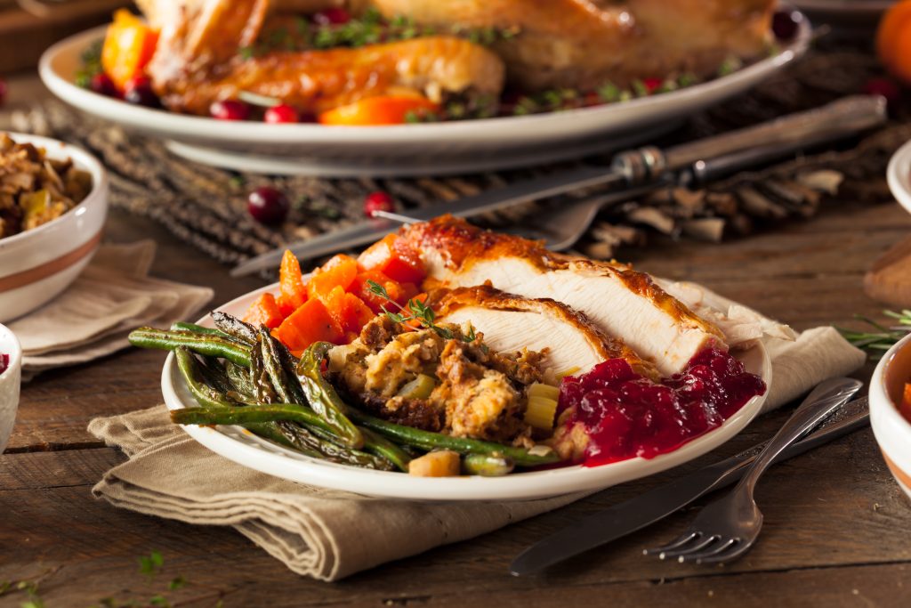 A table set for Thanksgiving. On the plate is turkey, stuffing, green beans, and cranberry sauce.